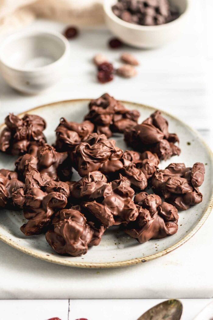 A small plate of chocolate almond nut clusters sitting on a marble cutting board.