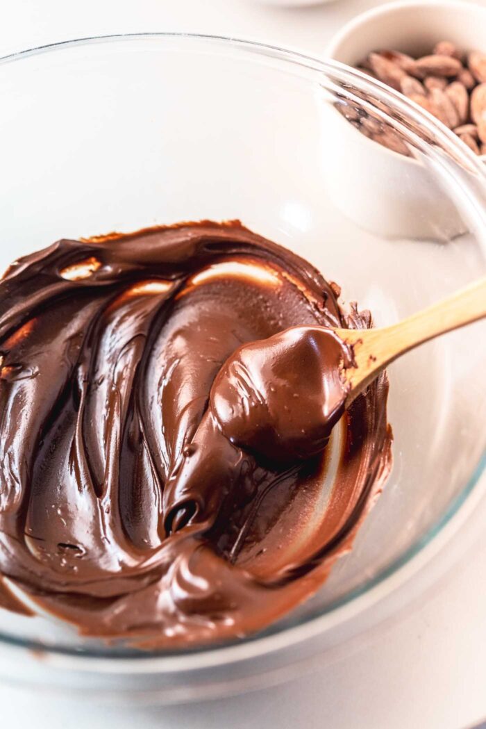 Melted chocolate in a glass mixing bowl with a small wooden spoon.