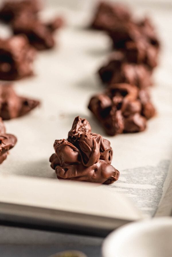 Close up of a chocolate nut cluster on a baking sheet lined with parchment paper with. more nut clusters in the background.