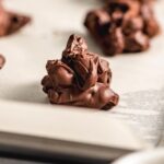 Close up of a chocolate nut cluster on a baking sheet lined with parchment paper with. more nut clusters in the background.