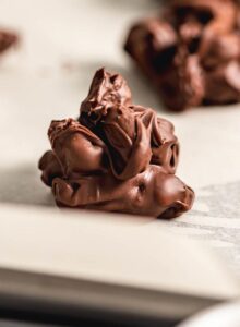 Close up of a chocolate nut cluster on a baking sheet lined with parchment paper with. more nut clusters in the background.