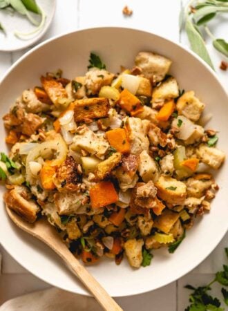 An overhead view of a bowl of butternut squash stuffing with bread, celery and herbs.