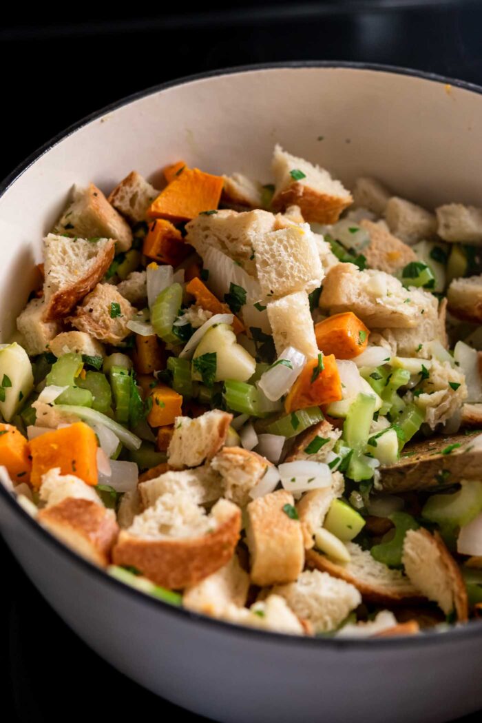 Cubes of bread, butternut squash and chopped onion, celery and apple mixed together in a large pot.