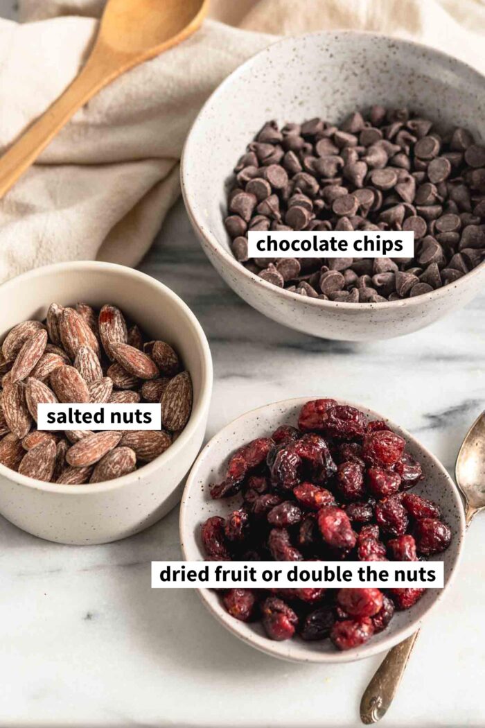 Bowls of salted almonds, dried cranberries and chocolate chips. Each ingredient is labelled with text overlay.