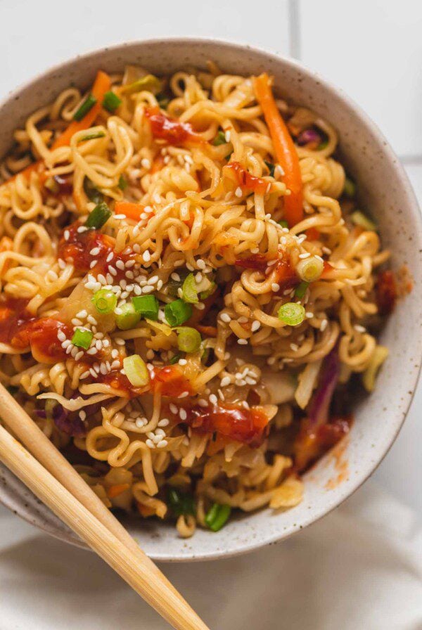 Overhead view of a bowl of pan fried ramen noodles with vegetables topped with sesame seeds and green onion.