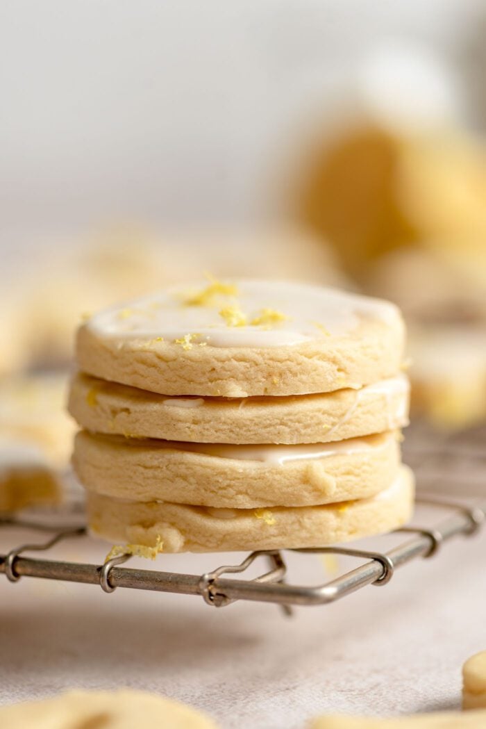 A stack of 4 small iced lemon shortbread cookies on a cooling rack.