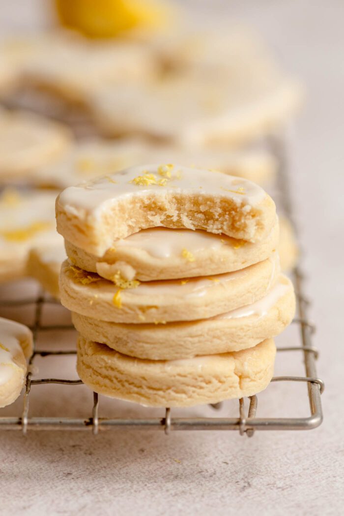 A stack of small, round lemon shortbread cookies with icing on a cooling rack. The cookie on top has a bite out of it.