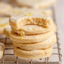 A stack of small, round lemon shortbread cookies with icing on a cooling rack. The cookie on top has a bite out of it.