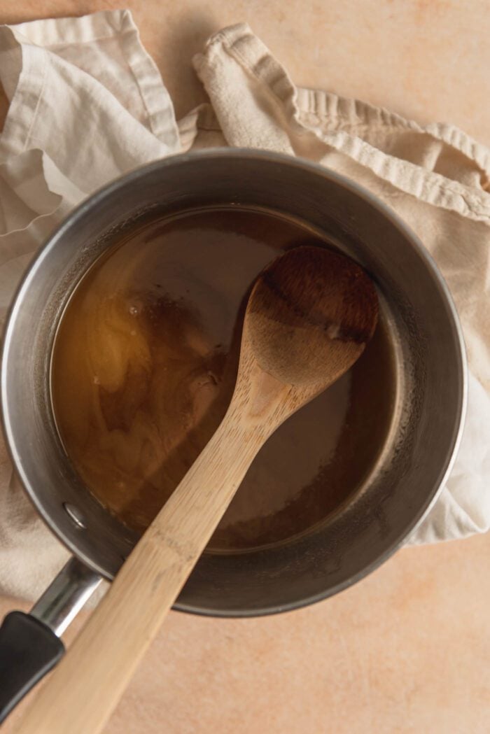 Melted butter mixed with brown sugar in a small pot with a wooden spoon resting in the pot.