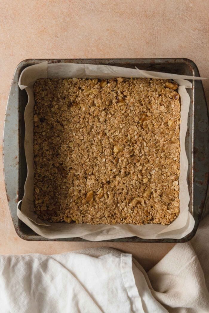 A layer of oat crust pressed into a square baking pan lined with parchment paper.