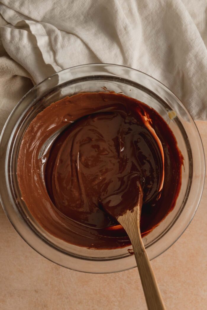Melted chocolate in a small glass mixing bowl with a small wooden spoon resting in it.
