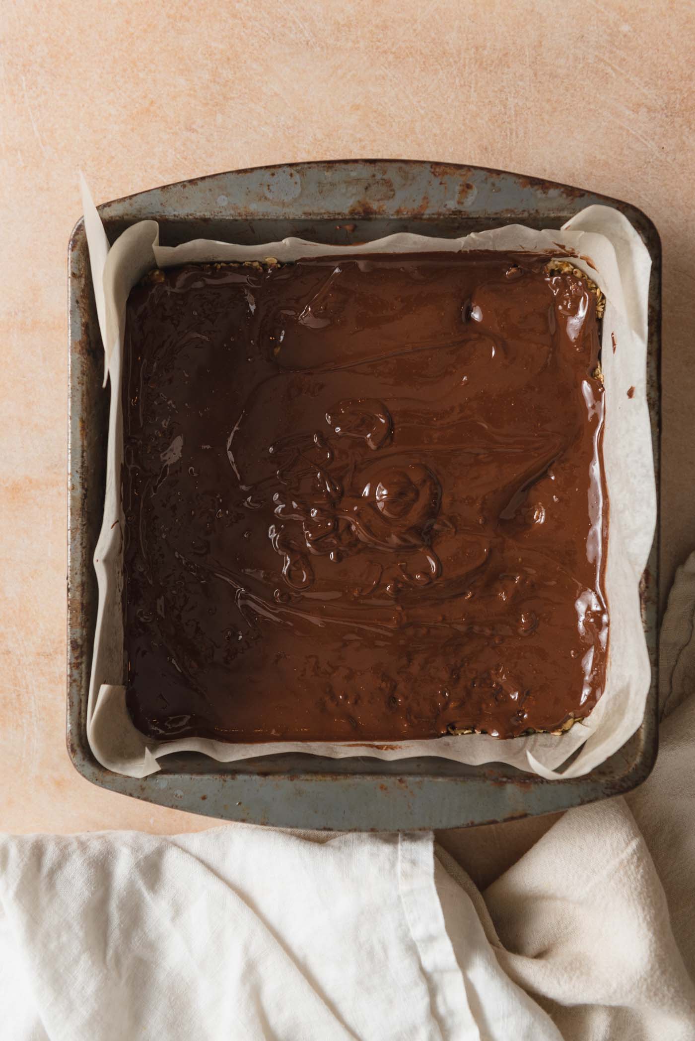 A layer of melted chocolate in a square baking pan lined with parchment paper.