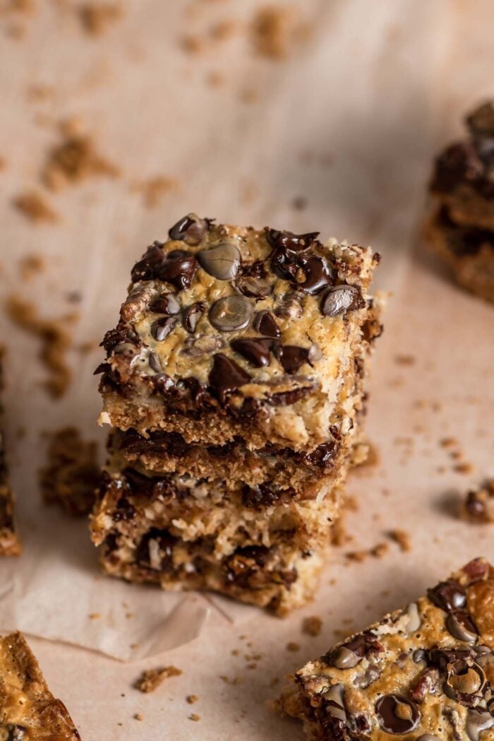 An angled view of a stack of 4 gooey 7 layer cookies bars with coconut, pecans and chocolate chips.