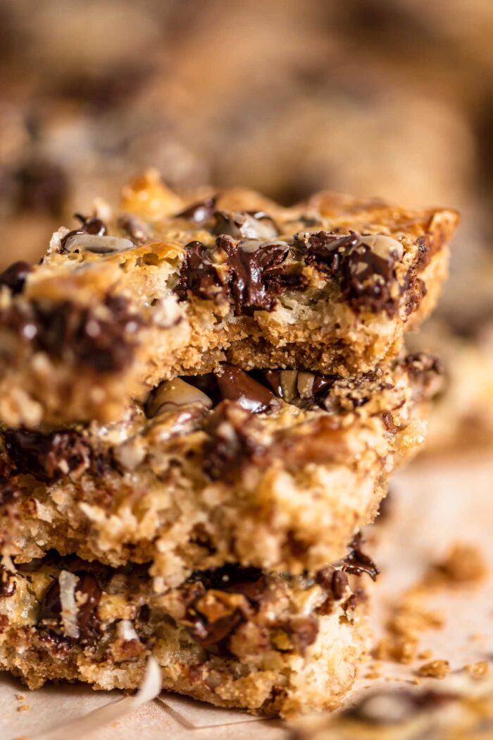 Close up of a seven layer magic bar with a bite out of it so you can see how gooey and decadent it is. There are chocolate chips, pecans and coconut on top of a graham cracker crust.