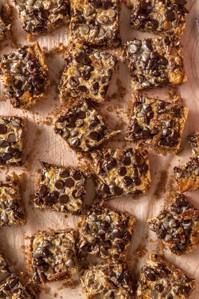 Overhead view of a batch of 7 layer cookies bars scattered on a counter. The bars are topped with chocolate chips, coconut and pecans.