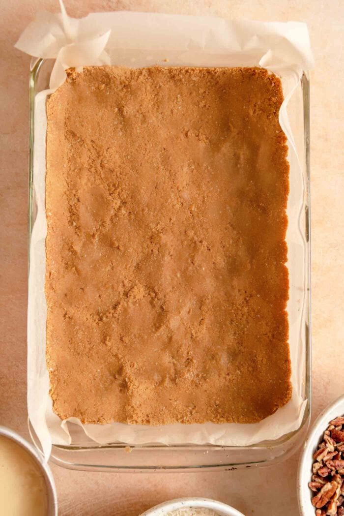 A layer of graham cracker crust pressed into a large 9x13-inch pan lined with parchment paper.