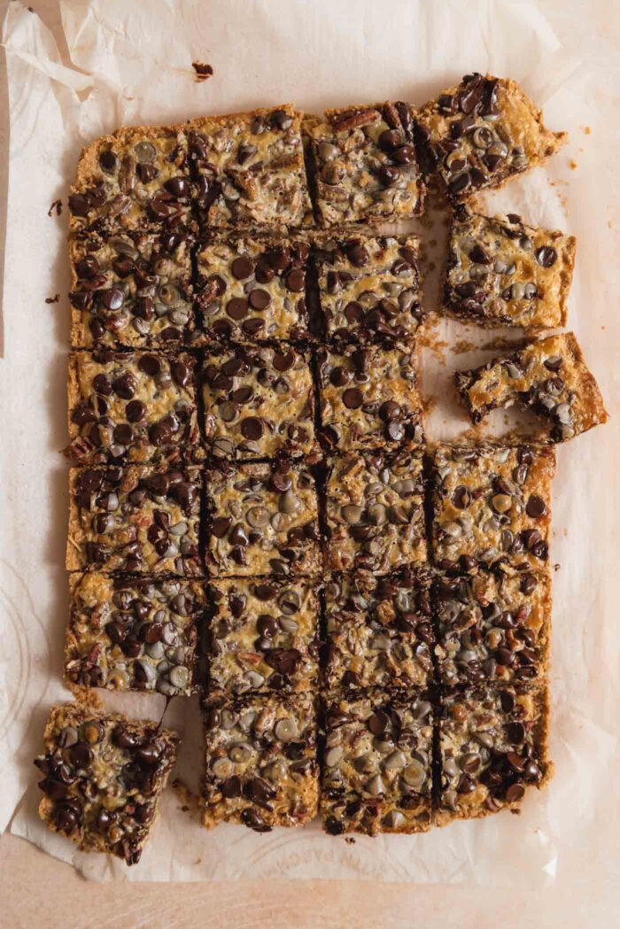 Overhead view of a pan of 7 layer cookies bars cut into 24 squares. A few pieces are pulled to the side and one has a bite out of it.