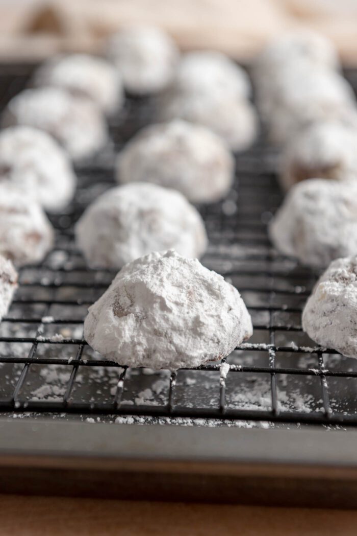 Close up of a snowball cookie on a baking rack placed over a baking sheet.