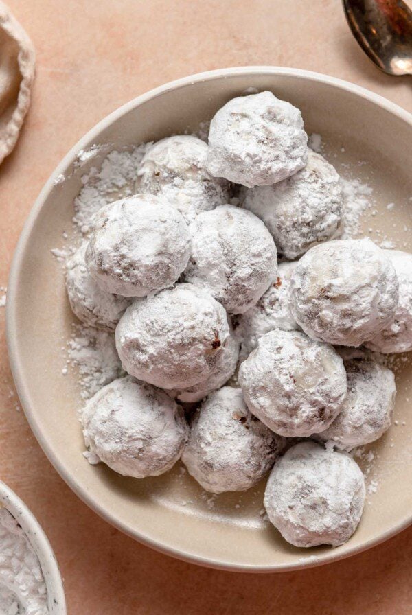 Overhead view of a bowl of powdered sugar-coated chocolate snowball cookies. A bowl of icing sugar can be seen just out of frame.