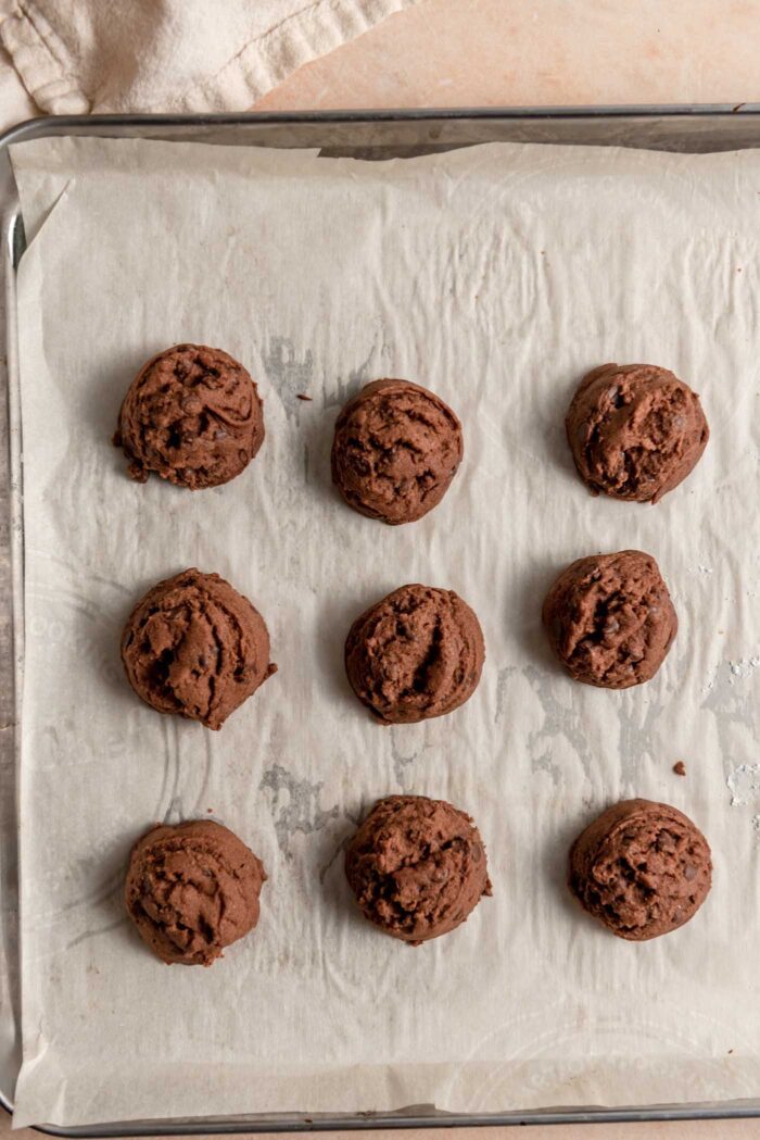 9 chocolate snowball cookies on a baking pan lined with parchment paper.