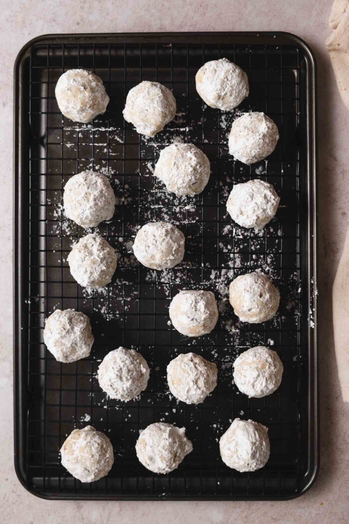 18 pecan snowball cookies on a baking cooling rack sitting on top of a baking sheet.