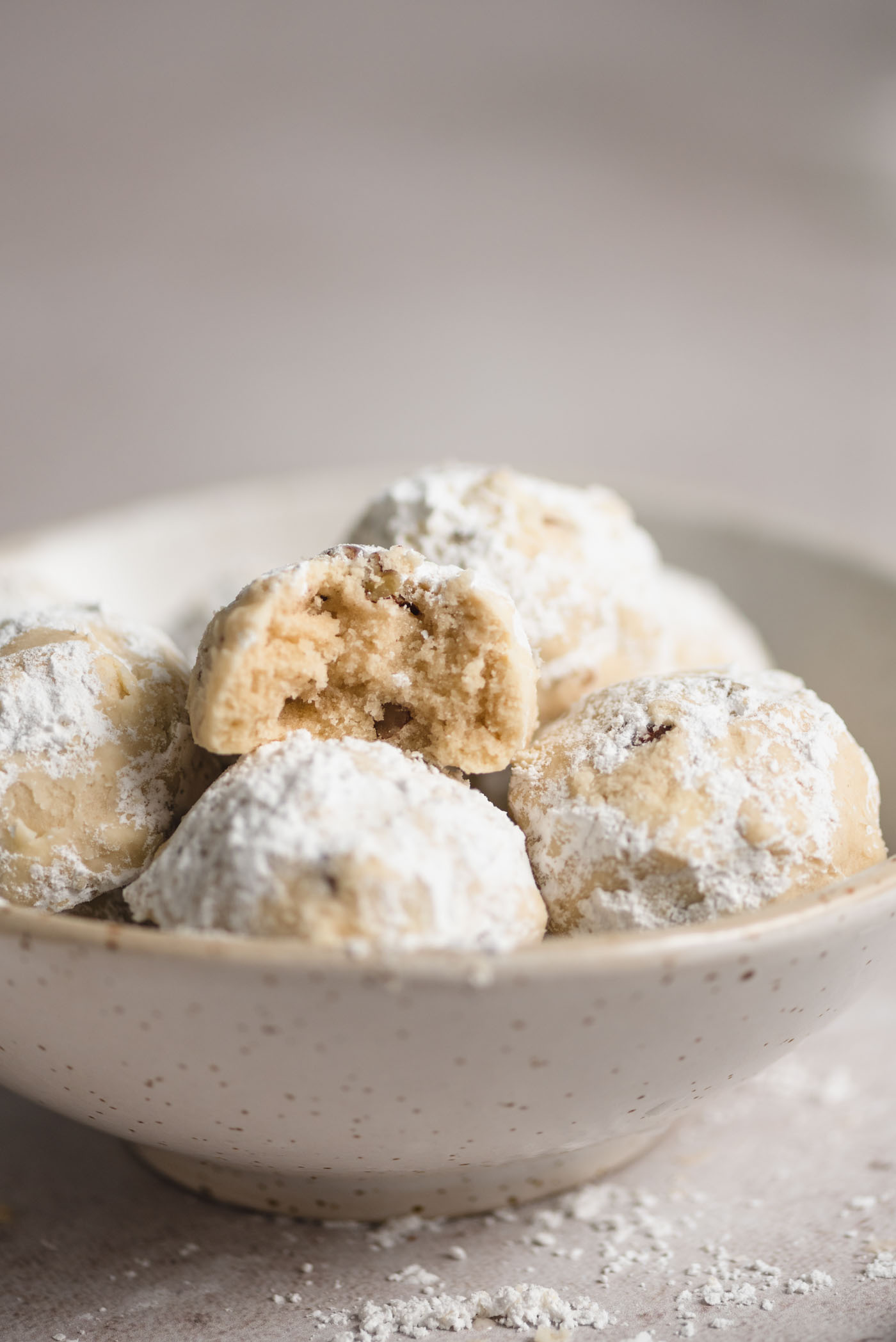 Pecan snowball cookies in a small bowl. The cookie on top has a bite out of it so you can see the inside texture.