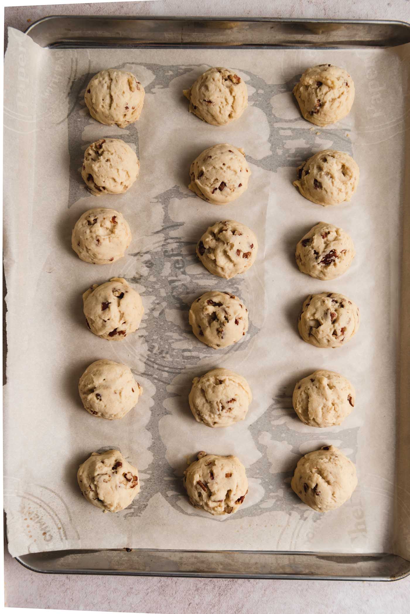 18 baked pecan snowball cookies on a baking tray lined with parchment paper.