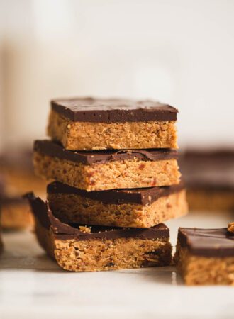 A stack of 4 chocolate peanut butter bars sitting on a marble cutting board with more bars in view in the background and foreground.