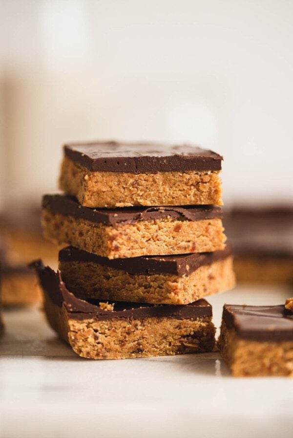 A stack of 4 chocolate peanut butter bars sitting on a marble cutting board with more bars in view in the background and foreground.