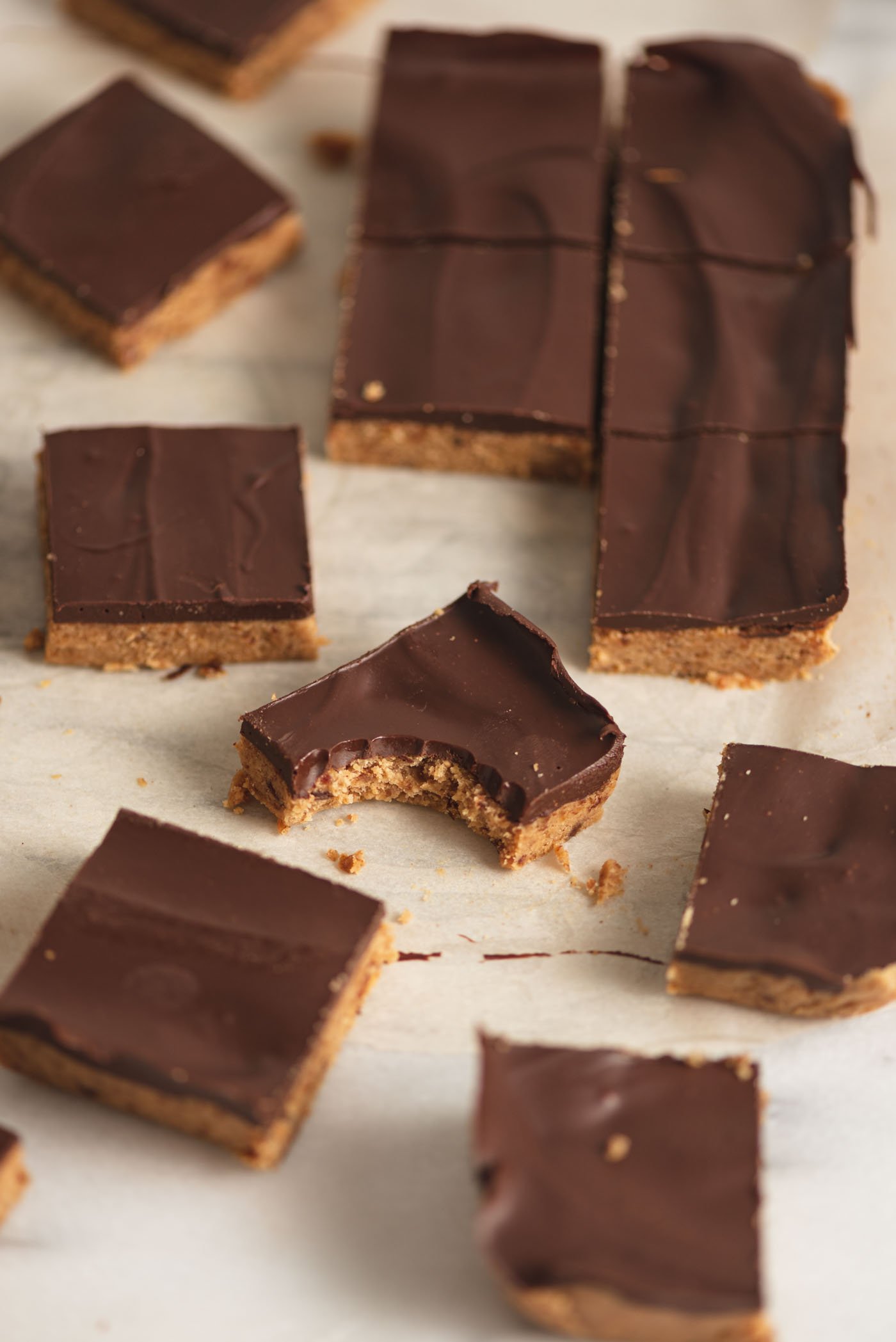 A number of chocolate peanut butter squares on a piece of parchment paper on a marble cutting board.