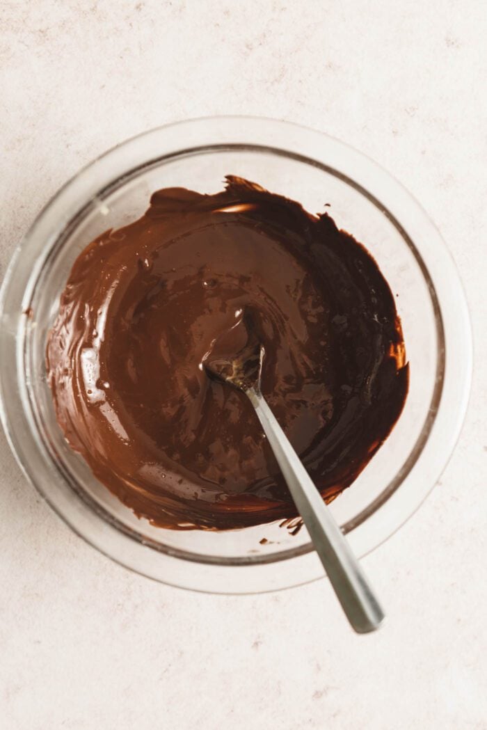Melted chocolate in a glass mixing bowl with a spoon in it.
