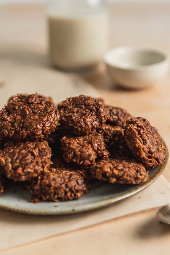 A plate of classic chocolate no-bake cookies with a small jar of milk in the background.