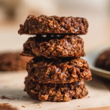 A stack of 4 vegan classic no-bake chocolate cookies sitting on a piece of parchment paper.