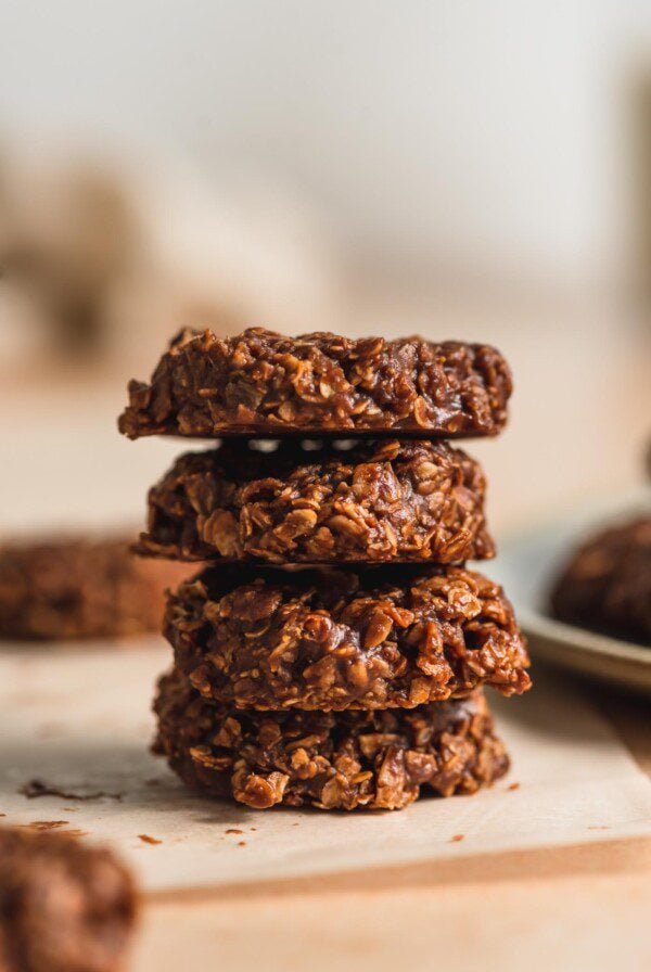 A stack of 4 vegan classic no-bake chocolate cookies sitting on a piece of parchment paper.