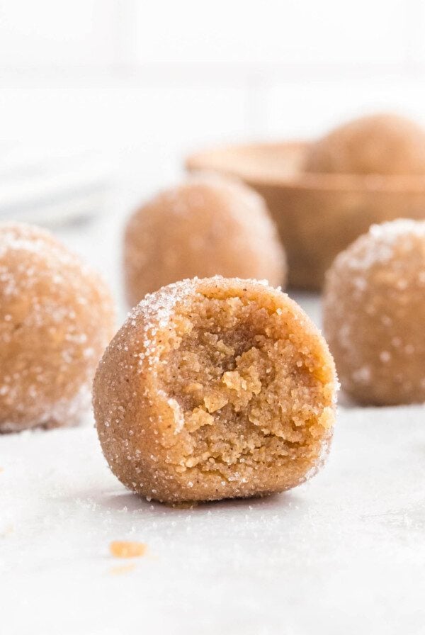 A ball of edible peanut butter cookie dough rolled in sugar with a bite out of it so you can see the inside texture.