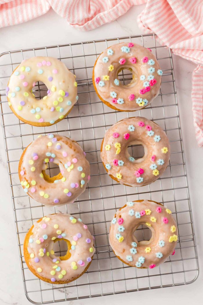 6 glazed donuts with sprinkles on a cooling rack.