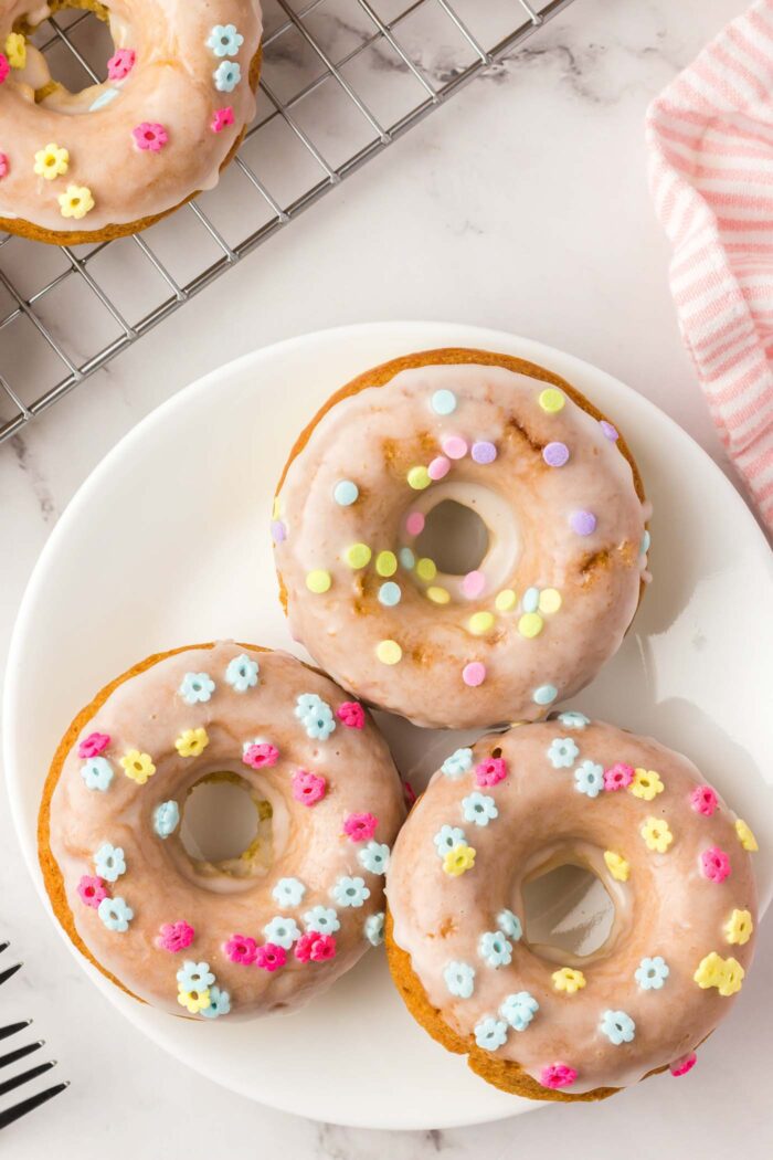 Three glazed donuts with sprinkles on a small plate.