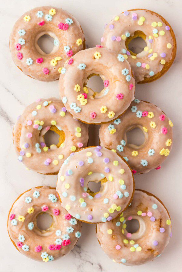 Overhead view of 8 baked and glazed donuts topped with small sprinkles shaped like flowers.