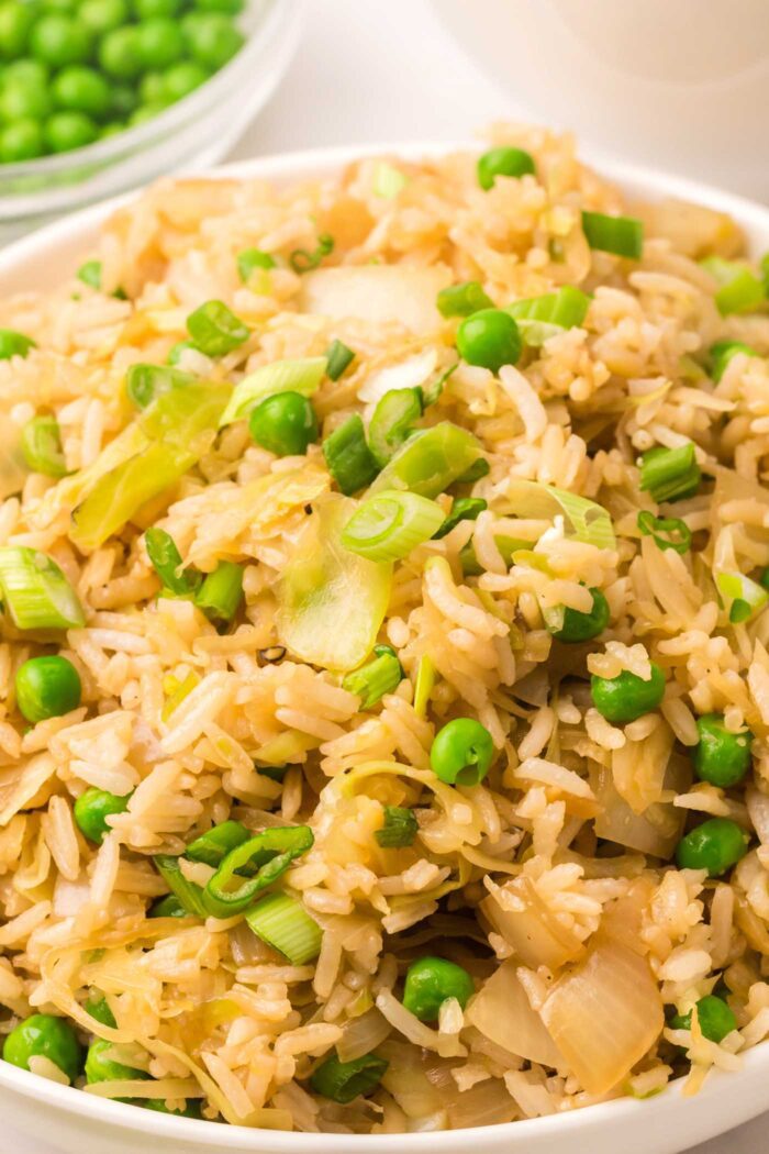 Close up a bowl of cabbage fried rice with peas and green onions.