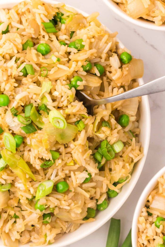 A bowl of cabbage fried rice with peas and onions with a spoon in it.