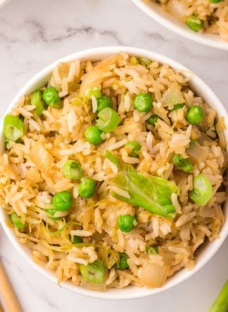 Overhead view into a bowl of cabbage fried rice with green onion and green peas.