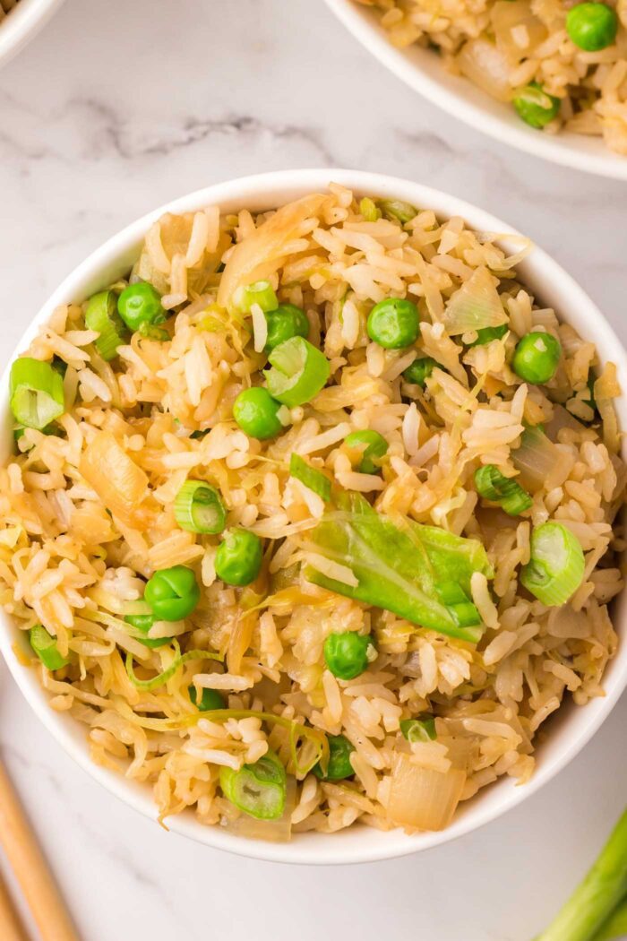 Overhead view into a bowl of cabbage fried rice with green onion and green peas.