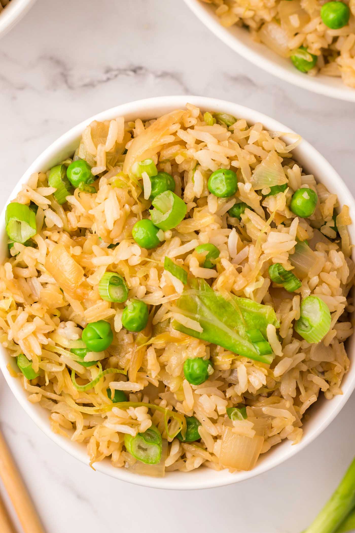 A bowl of cabbage fried rice with green onion and green peas.