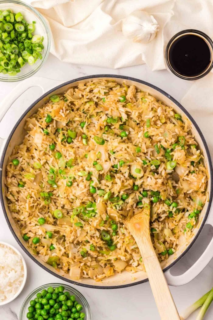 A large skillet of cabbage stir-fried rice with green peas and onions.