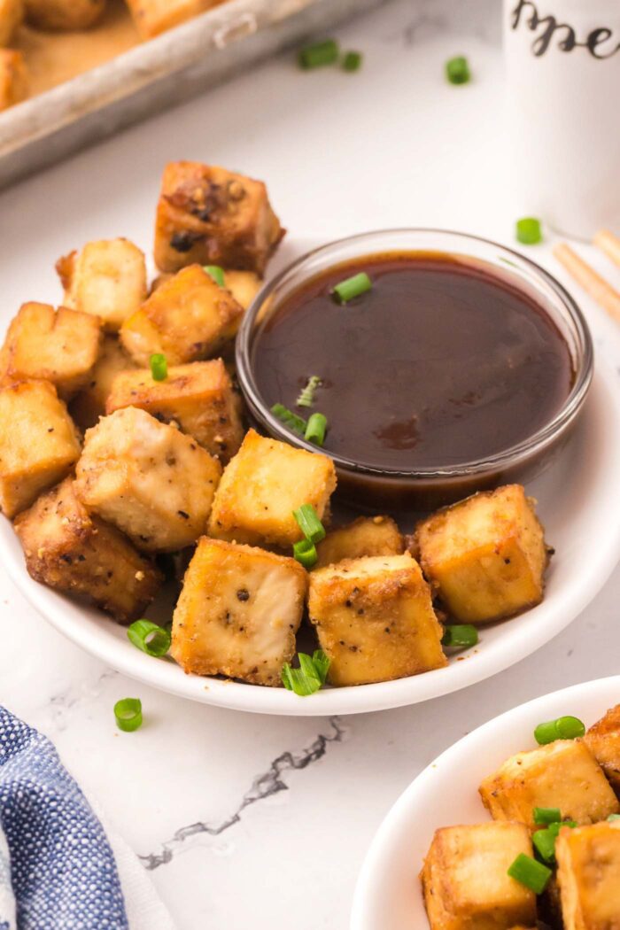 Cubes of crispy tofu on a plate beside a small bowl of dipping sauce.