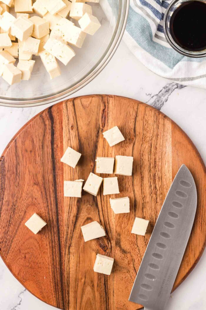 A number of cubes of firm tofu on a cutting board with a knife.