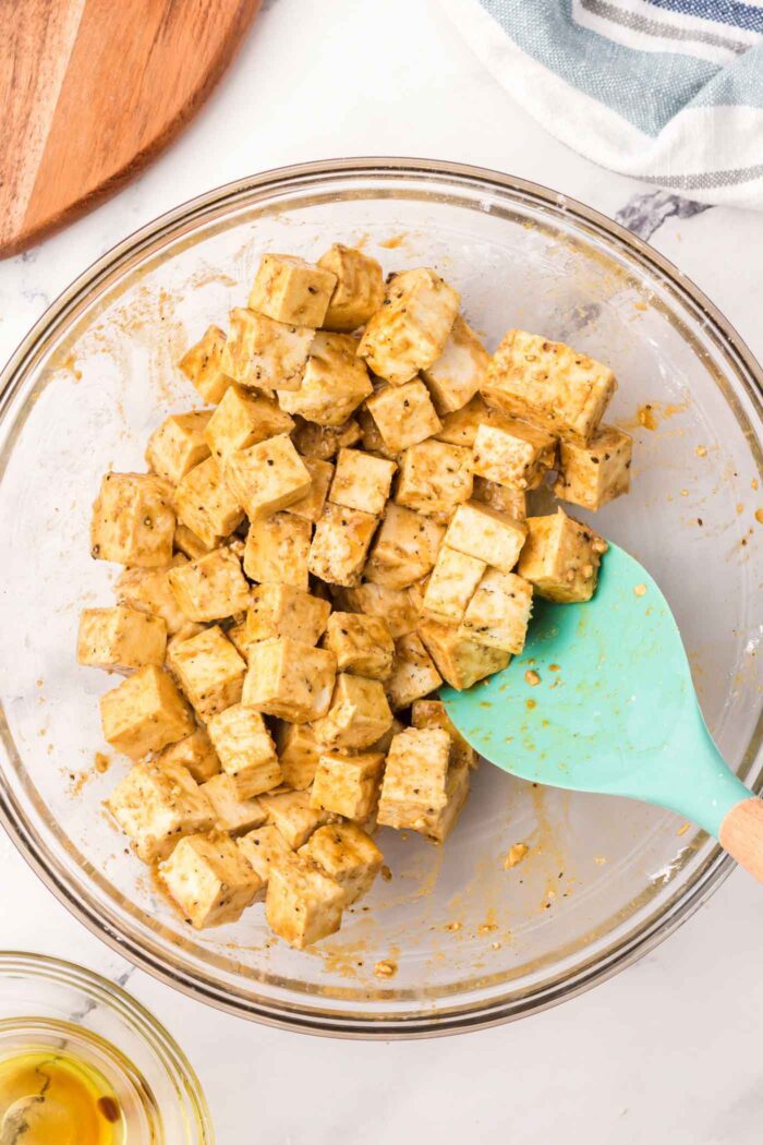 Cubes of tofu mixed with marinade in a bowl with a spatula in it.