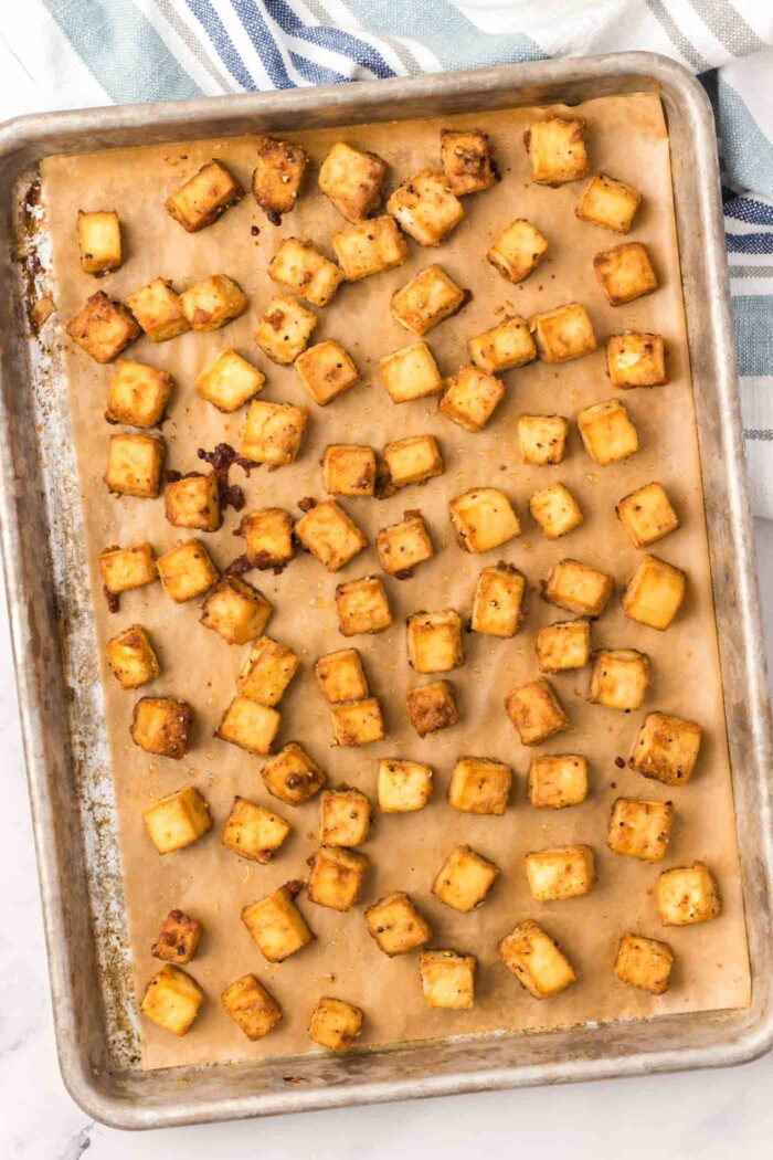 Cubes of crispy baked tofu on a baking sheet lined with parchment paper.