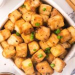 A big bowl of crispy baked tofu cubes sprinkled with green onion.