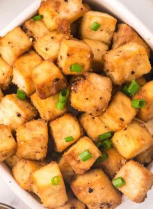 A big bowl of crispy baked tofu cubes sprinkled with green onion.